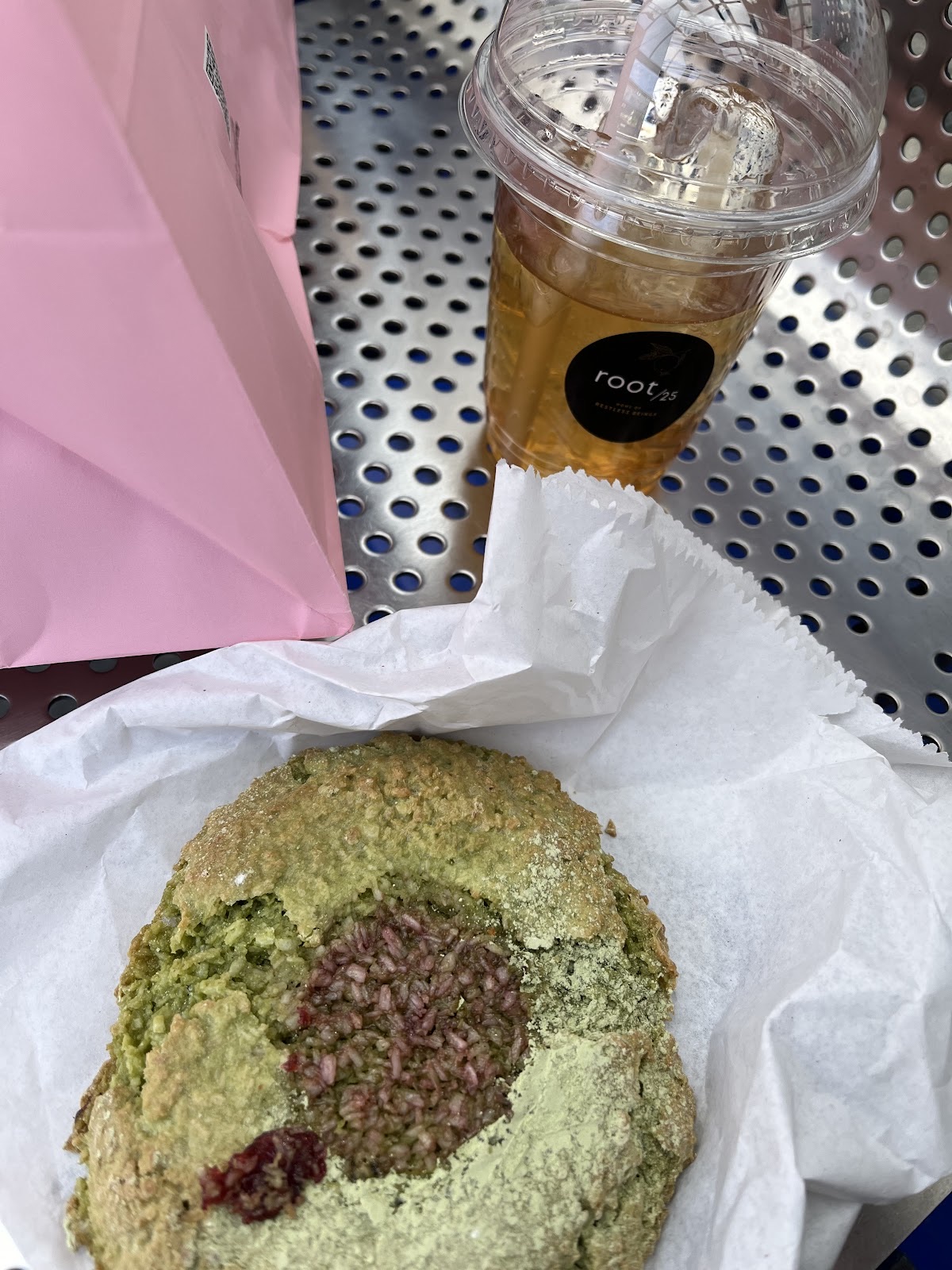 An iced coffee in a takeaway cup next to a pistachio-topped cookie on an outdoor table