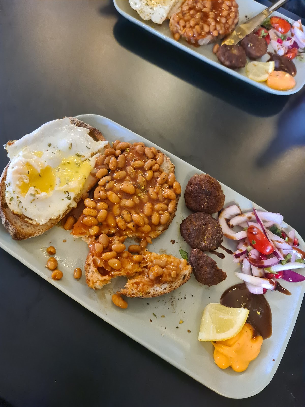 A full cooked breakfast with eggs, beans, sausage, hash and salad on a long white plate