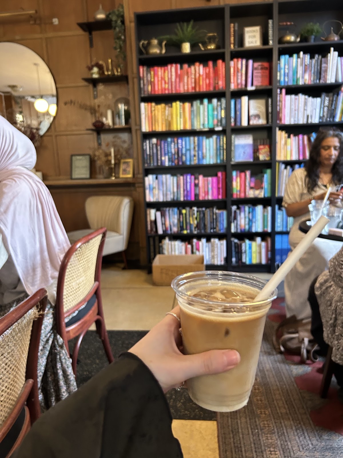 The rainbow-arranged bookshelf wall inside Root25, with customers seated among the shelves